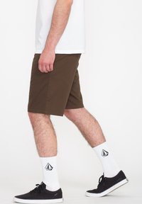 Brune bomulds shorts med lige pasform, båret med hvide knæhøje sokker og sorte sneakers. Enkel design, ingen synlige mønstre eller hardware.