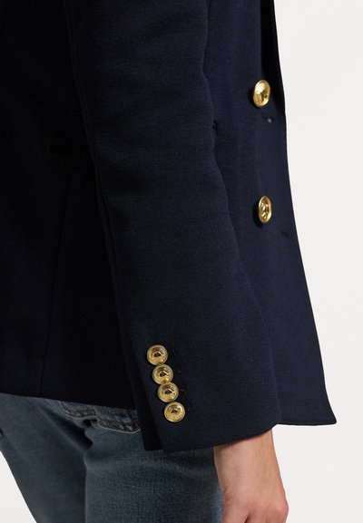 Blazer albastru marin cu un design ajustat, având nasturi de culoare aurie pe manșete și un material texturat. Croială slim, ajustată.