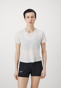 Hvit, tettsittende sporty topp med korte ermer og rund hals, sammen med svarte shorts. Stoffet virker lett og pustende.