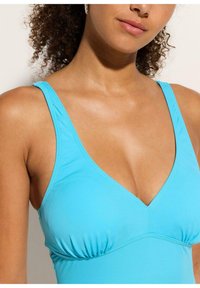 Un maillot de bain une pièce bleu clair avec un décolleté plongeant, doté de bretelles ajustables et de détails froncés sous la poitrine. Texture lisse.