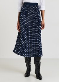 Jupe plissée bleu marine à pois blancs ; fabriquée en tissu léger. Elle possède une taille élastique et tombe jusqu'au milieu du mollet.