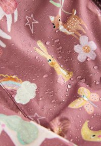 Tessuto rosa resistente all'acqua con motivi giocosi di conigli, cervi, fiori e arcobaleni, con gocce d'acqua sulla superficie.