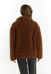 Brun, fuzzy jakke med en plysset tekstur, oversized pasform og bred krave. Bagsiden har et ensartet design uden synligt hardware eller accenter.