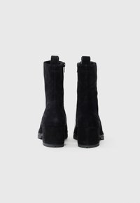 Botines de ante negros con un tacón grueso, que cuentan con una cremallera lateral y una lengüeta para facilitar su uso. Textura suave y diseño elegante.