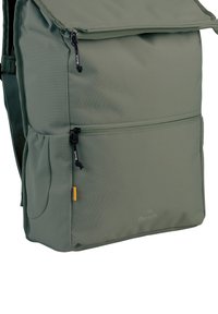 Sac à dos en tissu vert avec une poche zippée à l'avant, des bretelles réglables et un rabat de fermeture. Présente un logo subtil et des accents texturés.