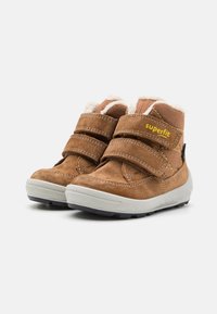 Brązowe zamszowe wysokie buty z białym futerkiem i podwójnymi rzepami. Posiadają szary gumowy spód z czarnymi akcentami. Logo "superfit" po boku.