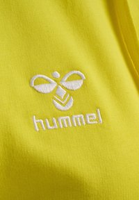 Tissu jaune vif avec un logo brodé blanc, comprenant un design de papillon stylisé avec le mot "hummel" en dessous.
