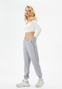 Pantalones de chándal grises con cinturilla y puños elásticos, combinados con un top corto blanco de hombros al descubierto. Modelo lleva zapatillas gruesas.