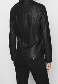 Giubbotto in pelle nera con pannelli trapuntati sulle spalle, design aderente, polsini con zip e un sottile dettaglio del logo sul retro.