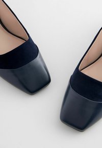 Navy syntetické kůže lodičky se čtveratou špičkou a kombinací hladkých a semišových textur na svršku. Minimalistický design a čisté linie.