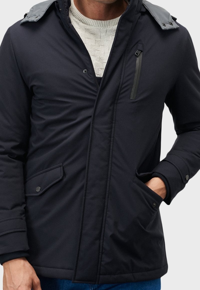 Svart vadderad jacka med dragkedja och tryckknappar. Har en kontrasterande krage och sidofickor, tillverkad i ett smidigt, vattenavvisande tyg.