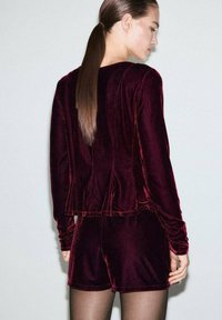 Set da lounge in velluto bordeaux composto da una maglietta a maniche lunghe e pantaloni shorts con vestibilità comoda. Tessuto liscio; cuciture e dettagli minimi.