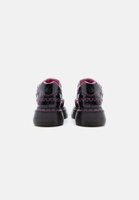 Μαύρα παπούτσια πλατφόρμα από δέρμα βινιλίου με παχιά ραβδωτές σόλες και ροζ ραφές, εμφανιζόμενα από πίσω σε λευκό φόντο.