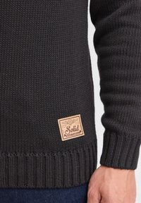 Pull en tricot gris foncé avec texture côtelée et une étiquette en tan portant la marque "Solid" sur le côté inférieur.