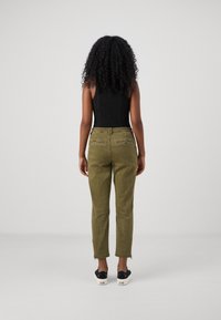 Olive green tapered pants with zippers at the hem, paired with a fitted black top. Material appears soft with a smooth texture.
