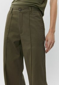 Olive green trousers made of smooth fabric, featuring a high waist, front pleats, and a button closure at the waist with side pockets.