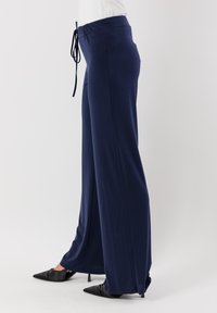 Pantaloni a gamba larga blu navy realizzati in un tessuto morbido, con una vita elastica dotata di cordoncino. I lati sono ampi per garantire comfort.