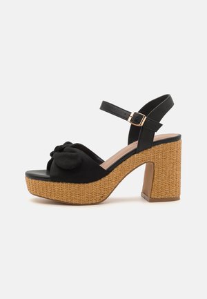 Sorte platform sandaler med en vævet jute hæl og en knyttet stofdetalje foran. Har en bageste ankelrem og en syntetisk sål.