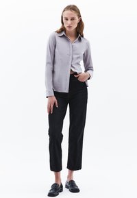 Camisa abotonada de un gris claro con cuello, combinada con jeans oscuros y mocasines negros. La tela es suave y el conjunto tiene una silueta ajustada.