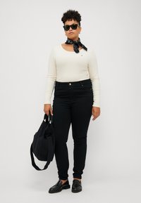Paita kremi cu mâneci lungi, blugi negri cu talie înaltă, pantofi negri slip-on și o geantă neagră. Include ochelari de soare și un eșarfă neagră cu model.