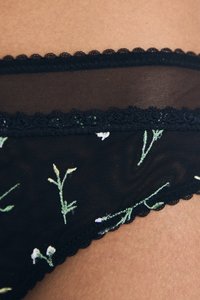 Zwarte doorschijnende lingerie met bloemembroidery in groen en wit, met een golvende kantafwerking langs de tailleband.