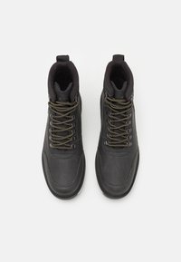 Botas impermeables negras con un acabado de piel suave, puntera redonda, cuello acolchado y cordones de color verde oliva. Presentan ojales reforzados y una suela texturizada.
