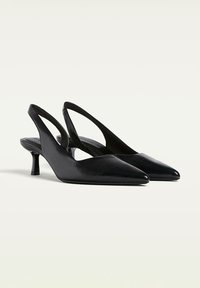 Les talons slingback en cuir noir présentent un bout pointu, un design épuré et un petit talon, avec un dos ouvert et des détails de découpes latérales.