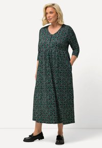 Vestido negro con estampado floral, escote en V, mangas tres cuartos y bolsillos; presenta patrones florales en verde y blanco. Combínalo con zapatos negros.