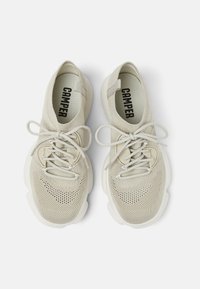 Beige Strick-Sportschuhe mit einem atmungsaktiven Mesh-Obermaterial, Schnürsenkeln und einer strukturierten weißen Sohle. Mit "CAMPER" auf den Innensohlen bedruckt.