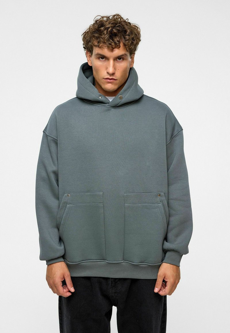 Hoodie in een gedempte groene stof met een gladde textuur, voorzien van twee voorzakken en gouden accenten. Ontwerp met een ontspannen pasvorm.