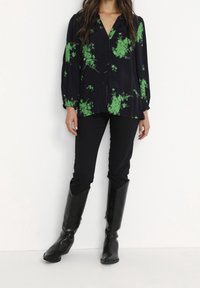 Blouse noire avec imprimé floral vert, manches longues, col, devant boutonné. Associée à un pantalon skinny noir et des bottes noires montantes jusqu'aux genoux.