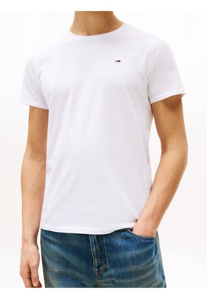 T-shirt en coton blanc avec un col rond, des manches courtes et un petit logo sur la poitrine gauche. Porté avec un jean en denim bleu.