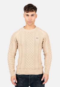 Beige kabelstickad tröja med ribbad rundhals och ärmslut. Har texturerade mönster och en liten logetikett längst ner fram.