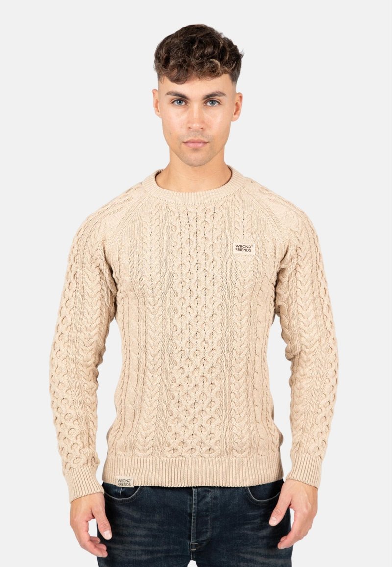Beige kabelstickad tröja med ribbad rundhals och ärmslut. Har texturerade mönster och en liten logetikett längst ner fram.