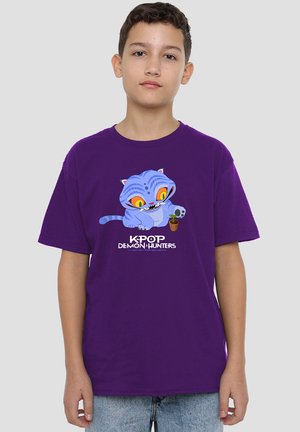 Boy wearing purple K-pop Demon Hunters T-shirt with a blue cartoon cat holding a small plant, standing against a plain background.