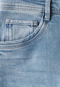 Vaaleansiniset farkut, joissa on etutasku, hienovarainen kuluminen ja ompeleet vyötärönauhassa ja taskussa, luoden tekstuurisen ilmeen.
