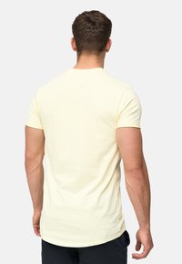 Camiseta de algodón amarillo claro con mangas cortas y cuello redondo, textura suave y un dobladillo trasero ligeramente más largo.