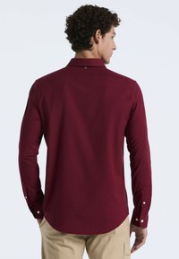 Langlopende bordeauxrode shirt met een button-down kraag, enkelvoudige knoopmanchetten en een gladde stoftextuur; beschikt over details op de achterkant bij de schouderpas.