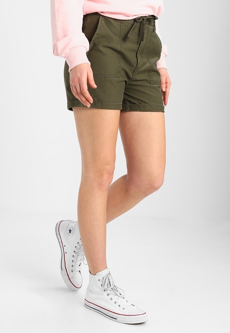 Olive green cotton shorts with a high waist, front pockets, and a drawstring. Paired with white high-top sneakers.