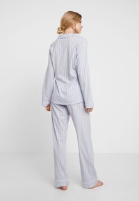 Randig pyjamas-set i ljusblått och vitt, med lång ärm, en kragad skjorta och matchande byxor. Tillverkat av bomull med pipade detaljer.