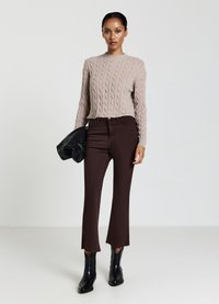 Pull beige en maille torsadée, jeans taille haute marron foncé avec bords bruts, bottines noires, et pochette noire.