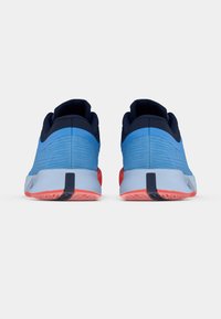 Siniset ja laivastonsiniset urheilusandaalit, joissa on rakenneverkko päällinen, sileä välipohja, punaiset yksityiskohdat pohjassa ja vetotappi takana.