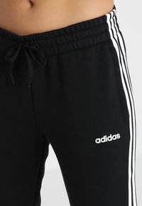 Zwarte Adidas joggingbroek met witte strepen aan de zijkanten, elastische tailleband met trekkoord, inclusief logo op de voorkant.