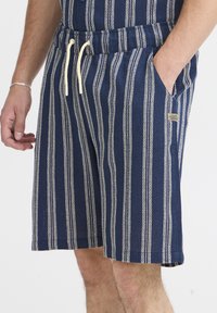 Pruhované námornícke šortky z bavlnenej látky. Majú šnúrku na stiahnutie v páse, bočné vrecká a textúrovaný vzor s bielymi pruhmi.