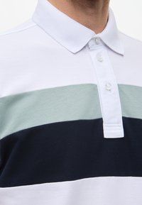 Polo-paita, jossa on valkoisia, vaaleanvihreitä ja tummansinisempiä vaakasuoria raitoja. Klassinen kaulus ja kaksi nappia, valmistettu teksturoidusta kankaasta.