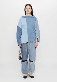 Denim-yhdistelmä, jossa on erivärisiä sinisen sävyjä ja paikkauskuvio. Pitkähihainen paita venepäänteellä, väljät housut, joissa on ainutlaatuisia yksityiskohtia.