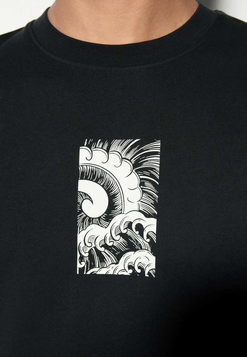 T-shirt noir avec un motif graphique rectangulaire blanc de vagues océaniques stylisées dans un design audacieux et détaillé en art linéaire.