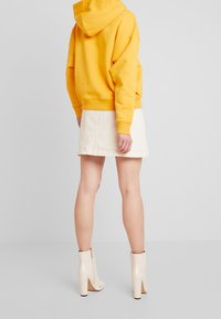 Sudadera amarilla con capucha y corte relajado, combinada con una falda de mezclilla color crema y botines de tacón beige con detalle de cremallera.