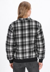 Fekete-fehér kockás bomber dzseki puha textúrával, bordás mandzsettákkal és aljjal. Galléros nyakkal és laza szabással a kényelem érdekében.