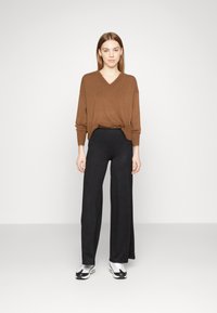 Bruine V-hals trui, losse fit, gecombineerd met lange zwarte broeken. Witte en zwarte sneakers maken de outfit compleet. Eenvoudig ontwerp, zachte textuur.